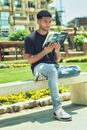 Man in Black Crew Neck T-shirt and Blue Denim Jeans Sitting on Concrete Bench Reading