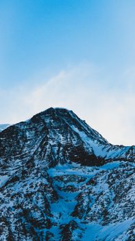 Majestic snowcapped mountain peak against a clear blue sky in winter, showcasing natural beauty.