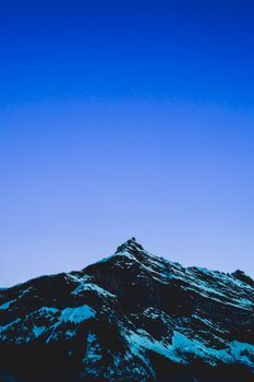 Snow-capped mountain peak with a clear blue sky, captured during twilight. Perfect for winter and nature themes.