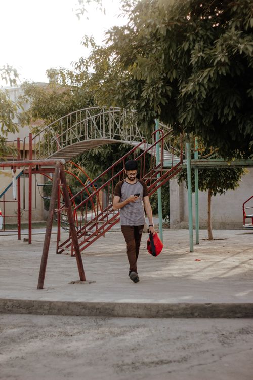 Free Adult male walking in park with phone, showcasing tech usage amid playground setup. Stock Photo