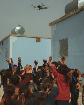 Joyful children playing outdoors, reaching skyward towards a flying drone.