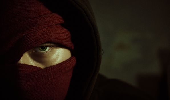 Close-up of a person with a red mask revealing only an eye, conveying mystery.