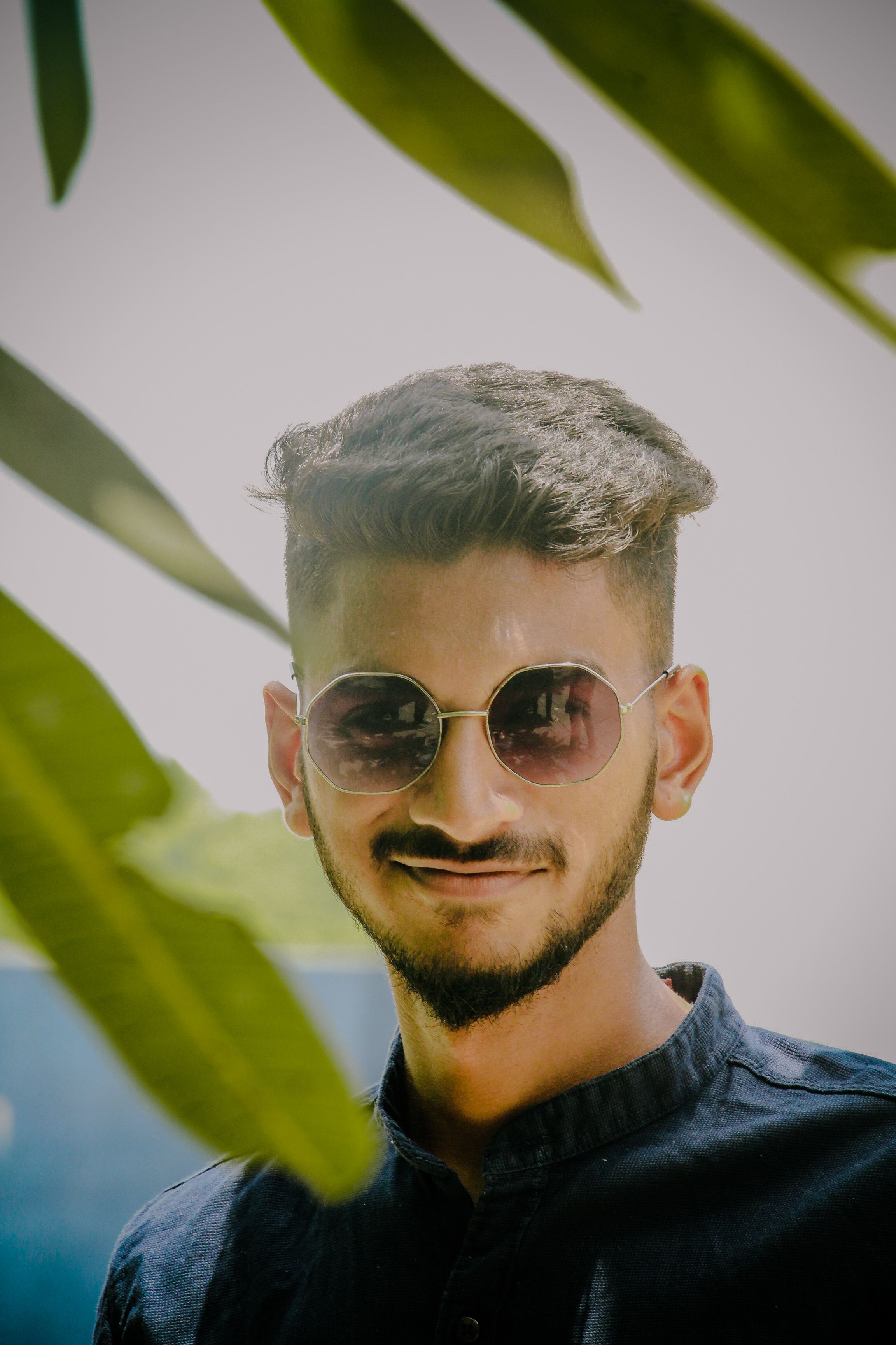 Portrait of a young man smiling in sunglasses with natural foliage background.