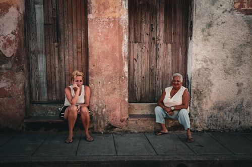 Free Two women sitting outside a weathered building enjoying a casual moment on a street Stock Photo