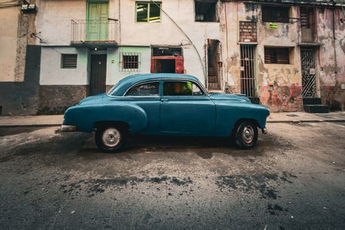Free Classic blue car parked on a vintage street with decaying buildings. Stock Photo