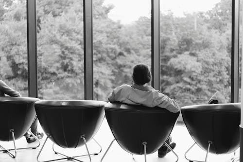 бесплатная Фотография в оттенках серого человека, сидящего на кожаном кресле и смотрящего перед дверью из прозрачного стекла Стоковое фото