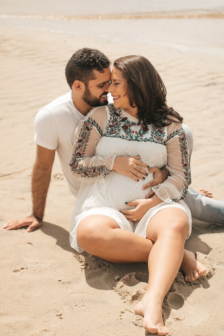 Expecting Couple Sitting On Beach