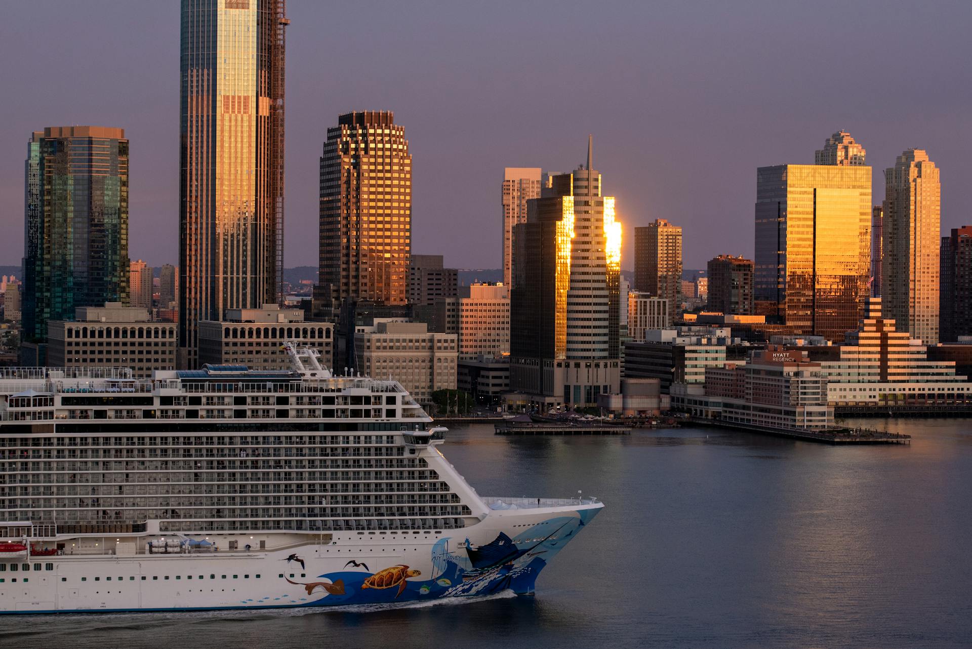 Stunning view of a cruise ship passing by the sunlit New York City skyline at sunset.