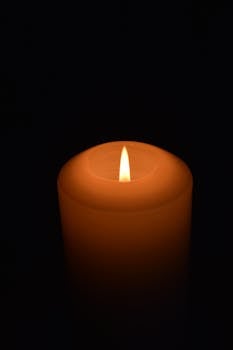 Close-up of a candle with a bright flame, creating a serene atmosphere in darkness.