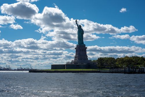 Free Iconic Statue of Liberty with vibrant blue sky and white clouds in New York City. Stock Photo