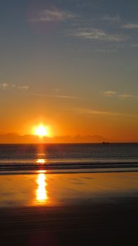 A captivating sunrise over a calm sea with golden reflections on the sandy shore.