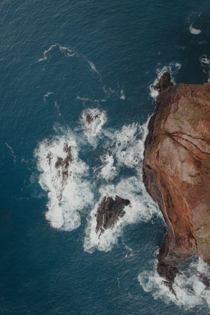 Dramatic aerial shot of waves crashing against the rocky cliffs of Madeira's coastline.