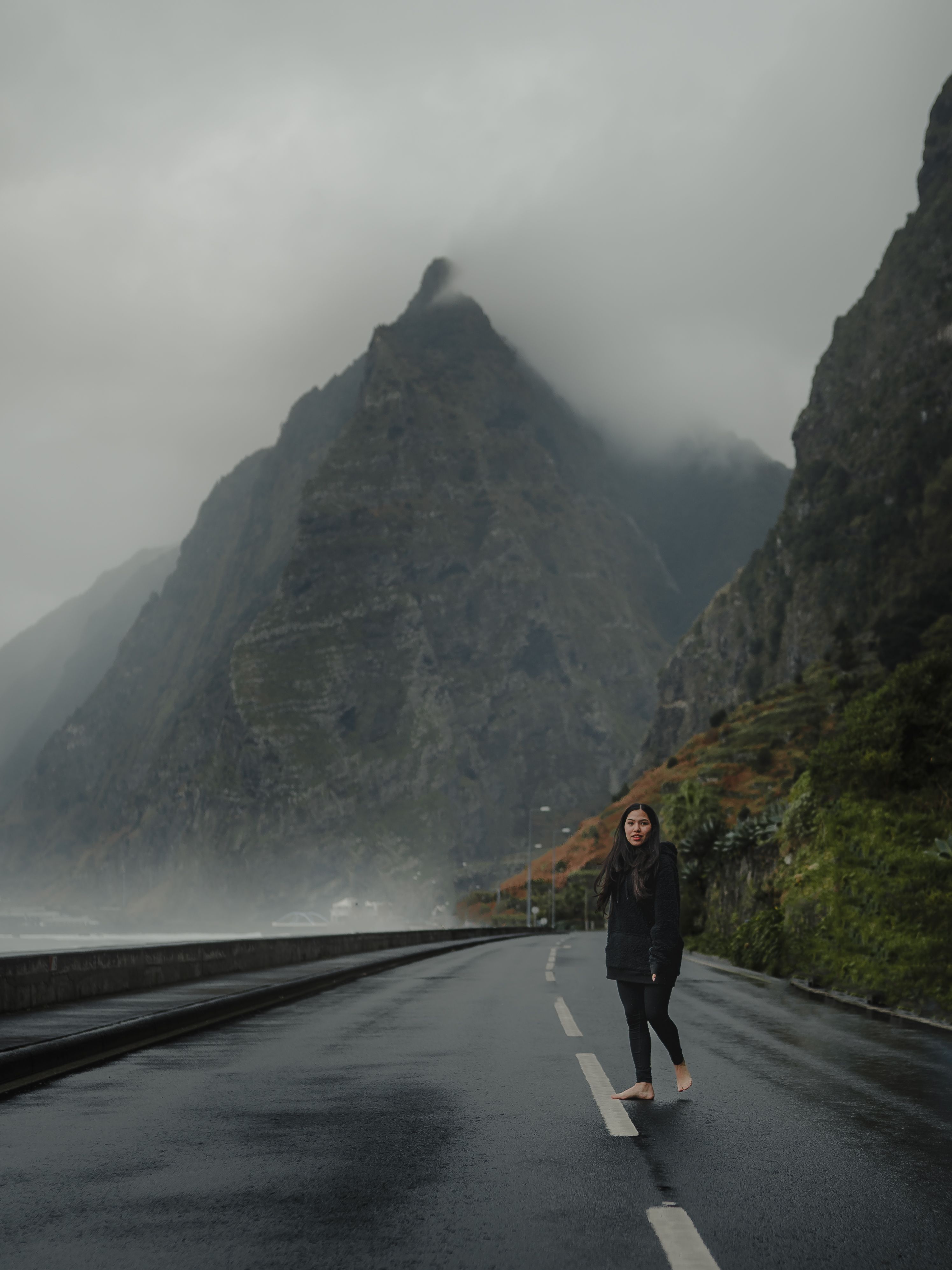 Dramatic mountain landscape with a misty road and a woman walking, capturing a serene travel moment.