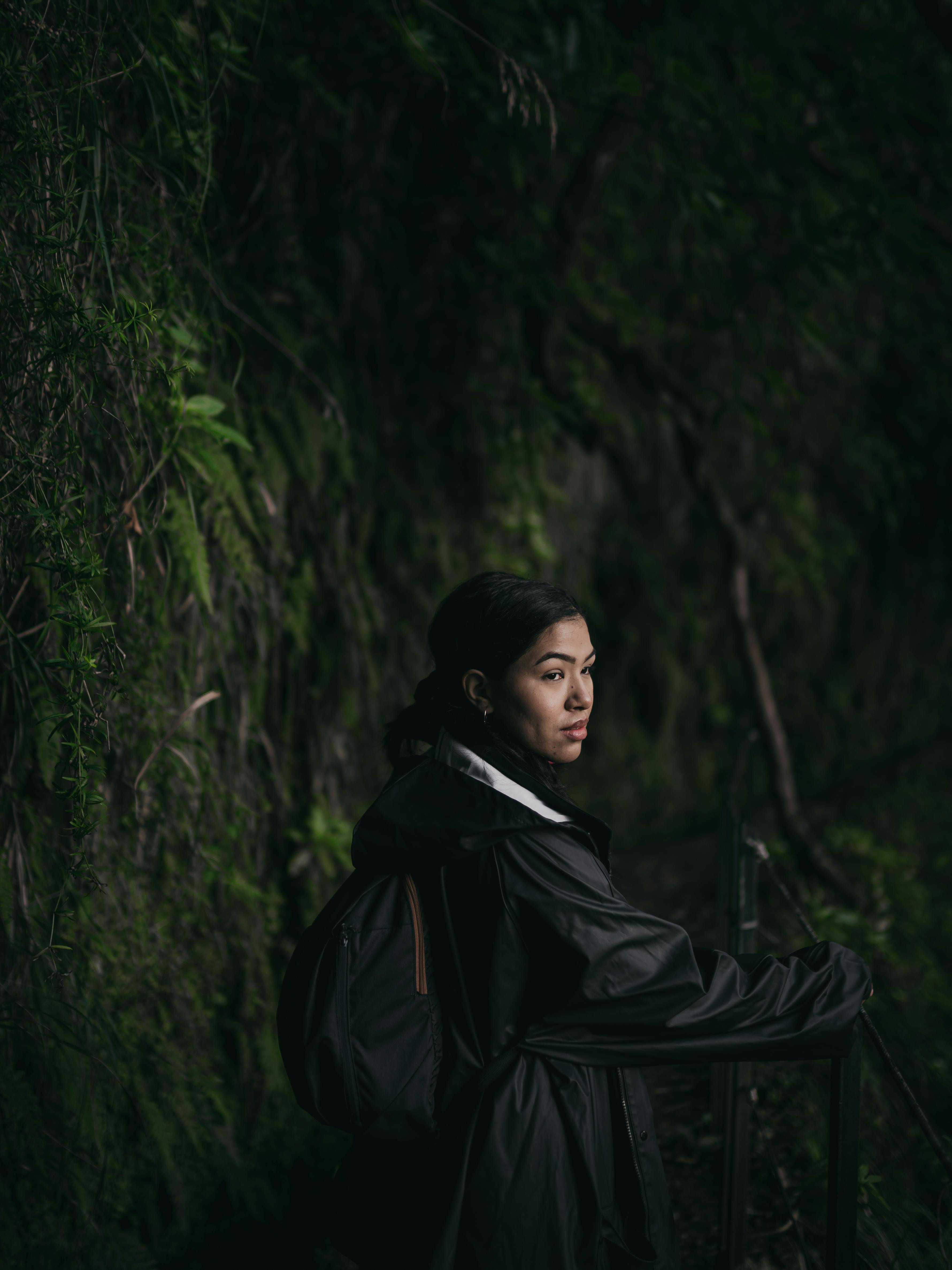 A woman with a backpack on a dark, lush forest path, highlighting adventure in nature.