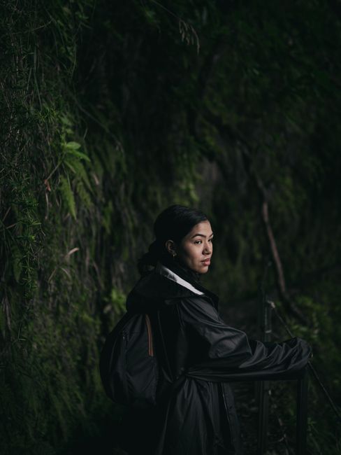 A woman with a backpack on a dark, lush forest path, highlighting adventure in nature.