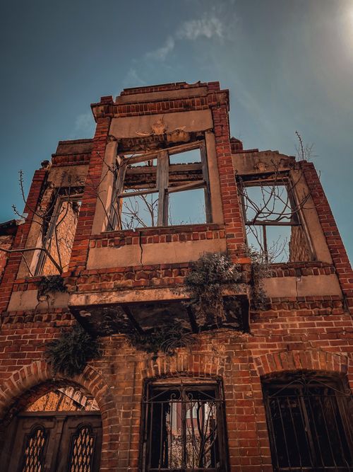 Free A damaged brick building with open windows under a clear blue sky. Stock Photo
