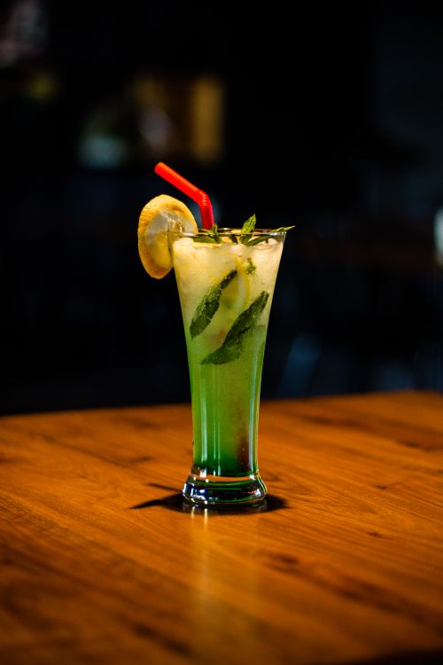 Free Tall glass with a green cocktail garnished with mint and lemon on a wooden table. Stock Photo