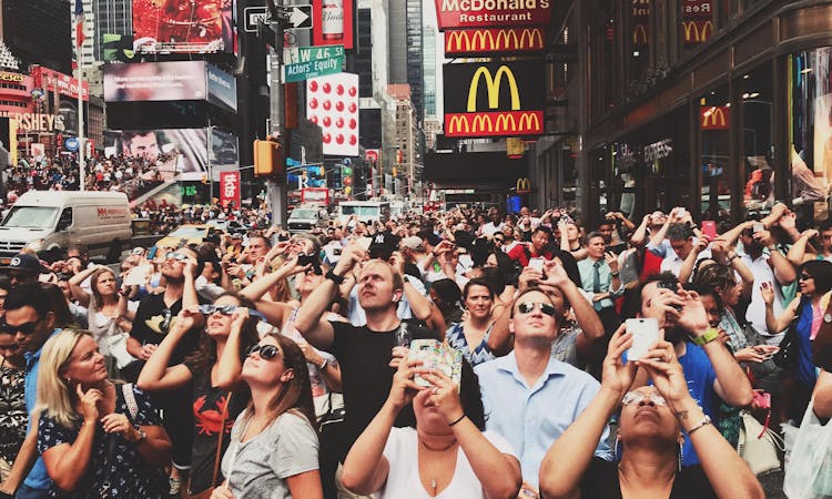 Crowd Of People In A City Looking At Up And Taking Photographs