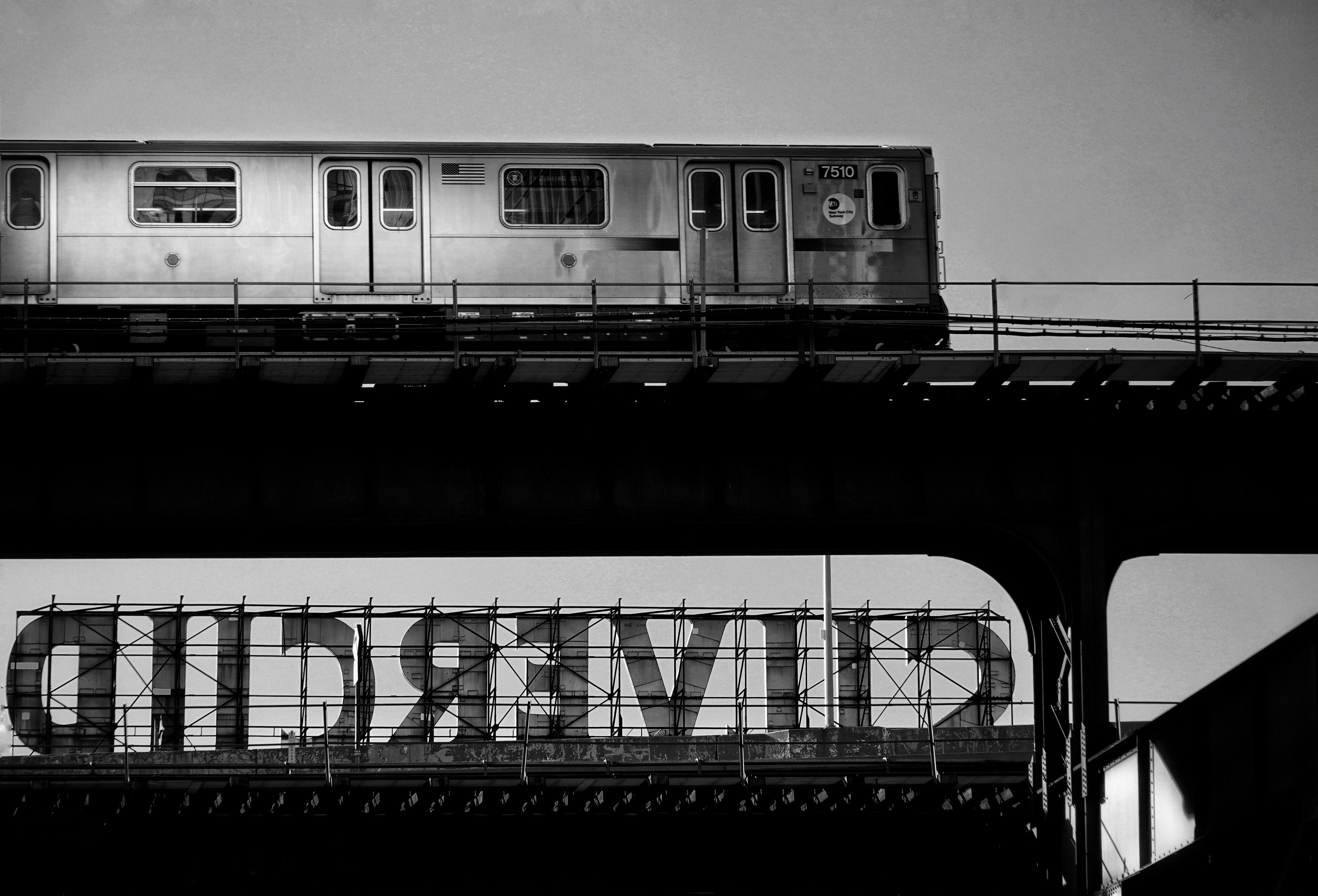 Black and white image of a train on an elevated track in an urban setting, illustrating public transportation.