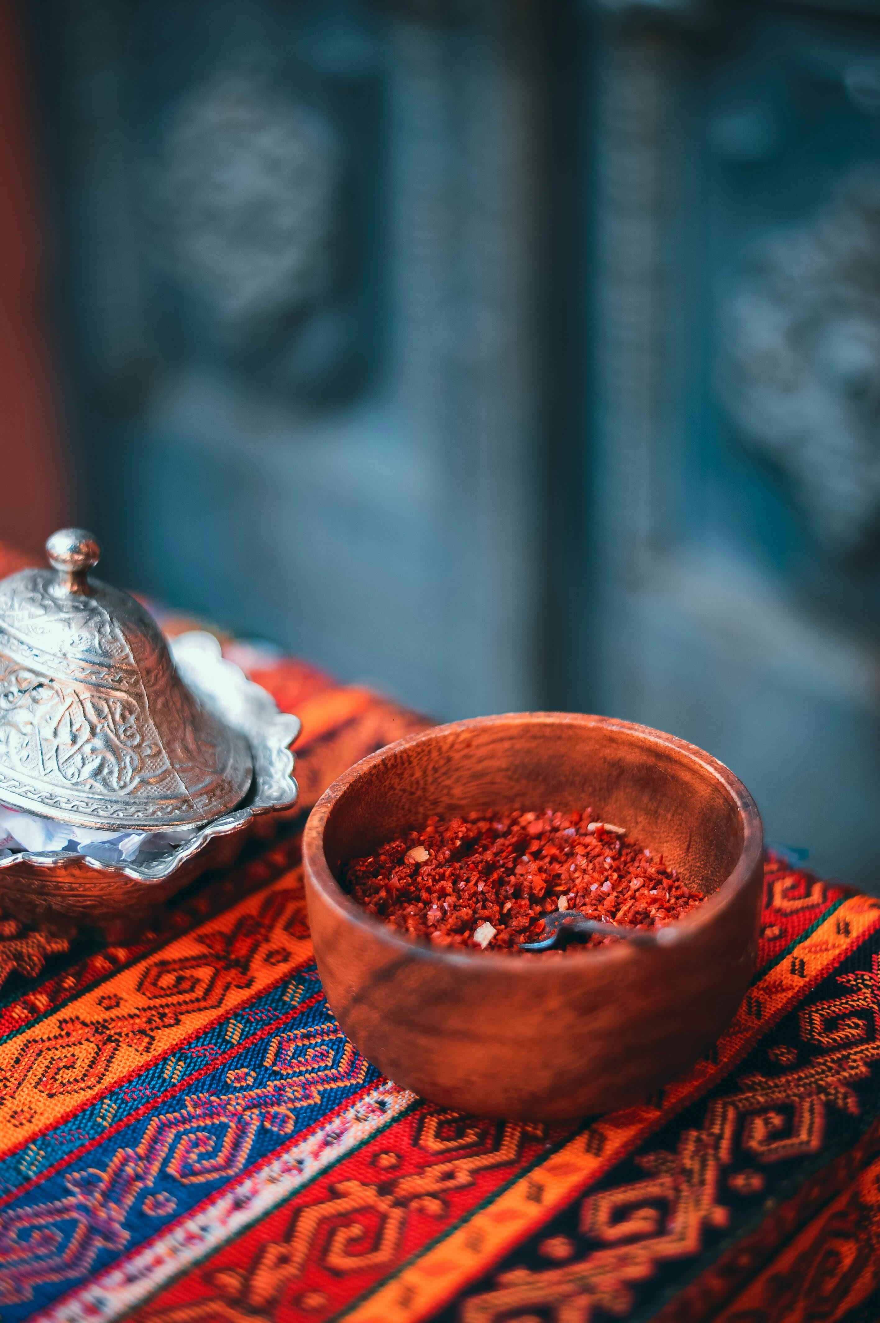 Close-up of a wooden bowl filled with spices on a colorful patterned cloth, exuding a warm and rustic vibe.