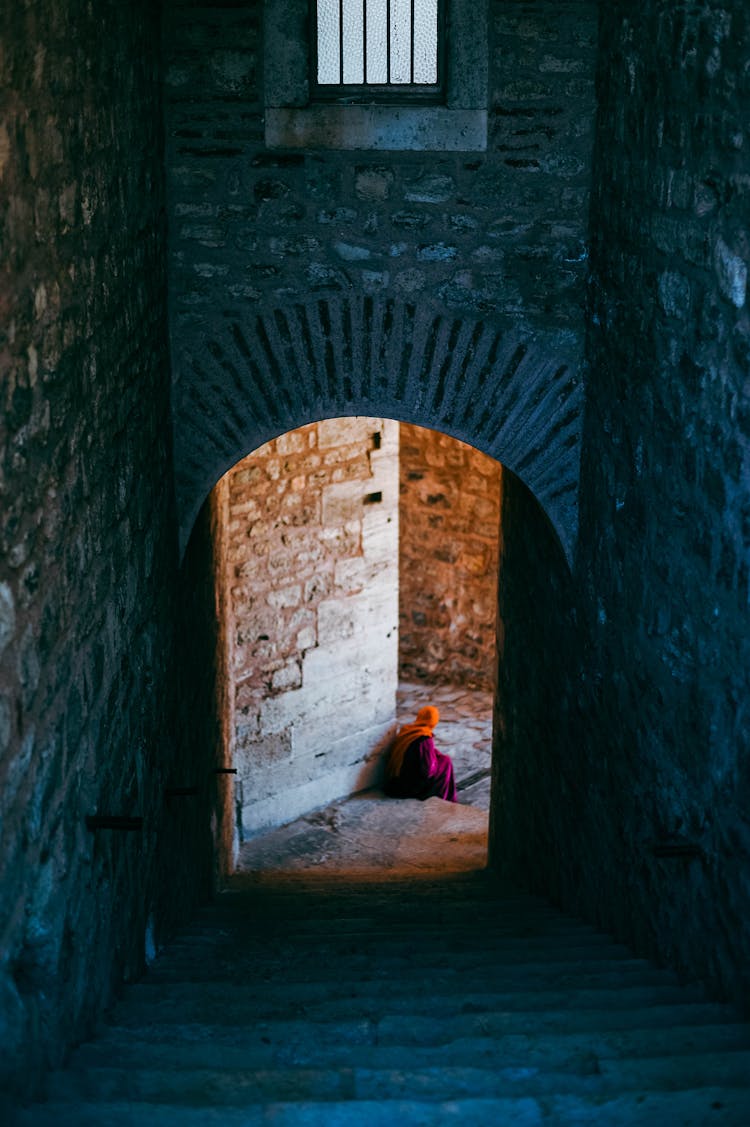 Photo Of A Stone Interior With Stairs And An Arch Entrance And A Person Sitting At The Bottom Of The Stairs