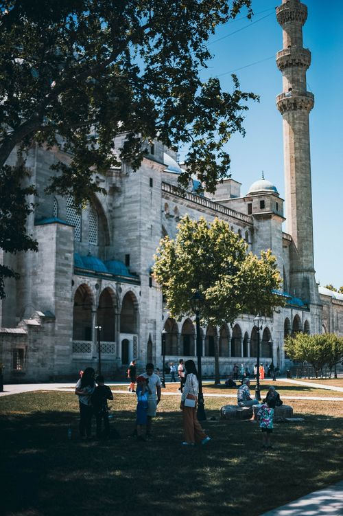 Free A group of people enjoying a sunny day in a park near a historic mosque with a tall minaret. Stock Photo