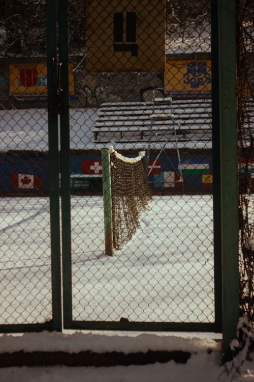Free A snowy tennis court seen through a metal gate with flags and snowbanks. Stock Photo