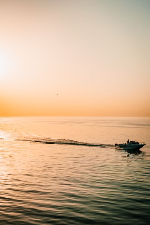 Free A motorboat cruises on calm waters under a warm sunset sky, creating a tranquil scene of oceanic beauty. Stock Photo