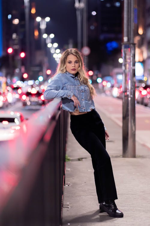 Woman Wearing a Crop Denim Jacket and Black Pants Leaning on a Railing