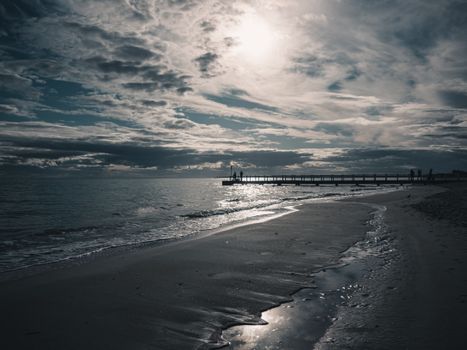 Tranquil evening beach scene at sunset with silhouetted pier and calm waves.