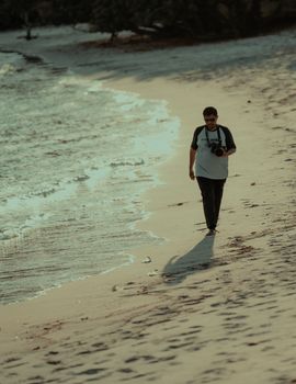 Man with camera walking on a tranquil sandy beach under warm daylight.