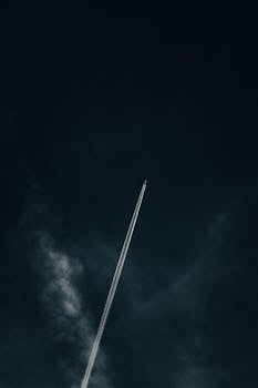 A high-flying airplane leaves a contrail in a dark night sky, creating a striking visual contrast.
