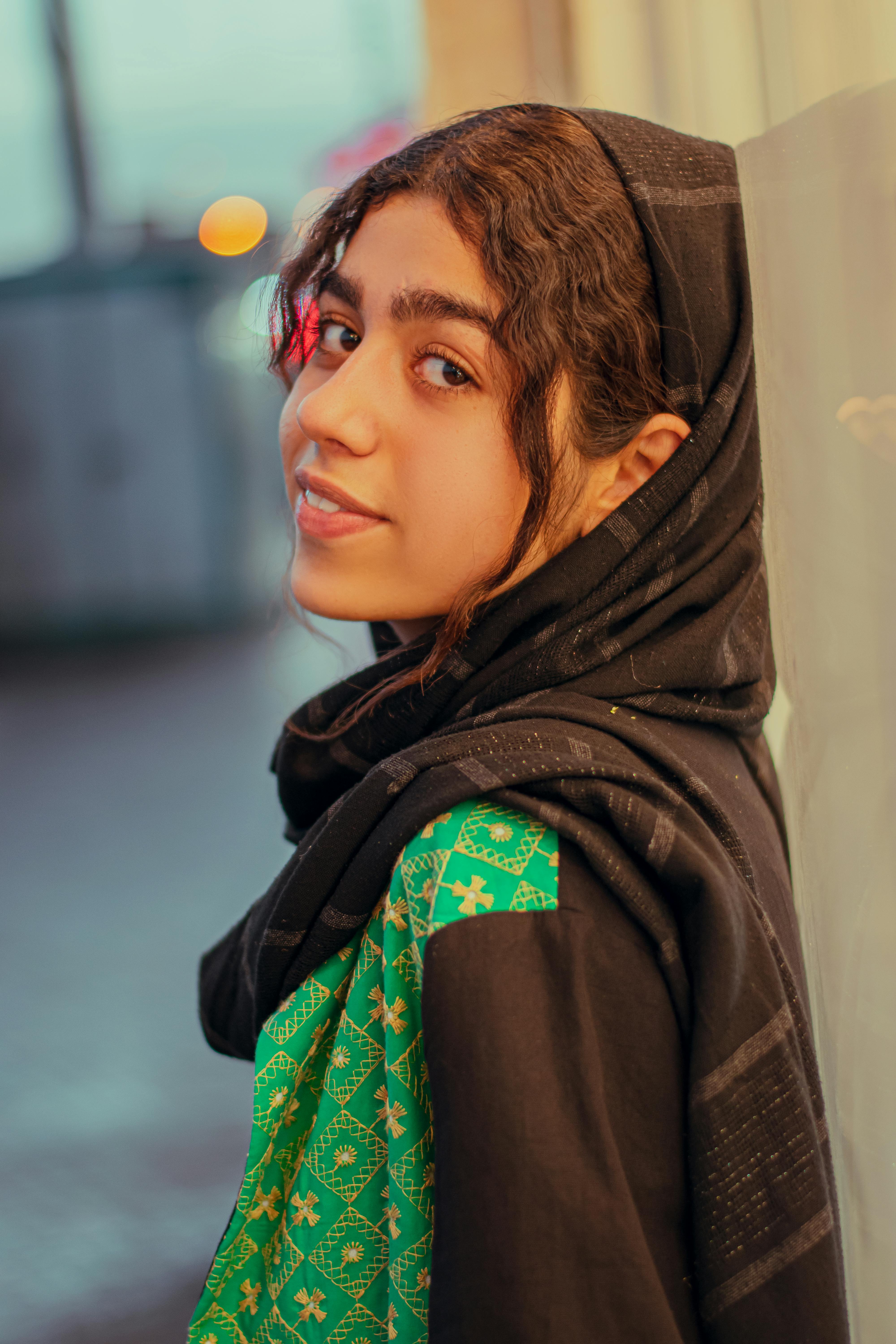 A young woman with curly hair in traditional dress leans against a wall in Jiroft, Iran.