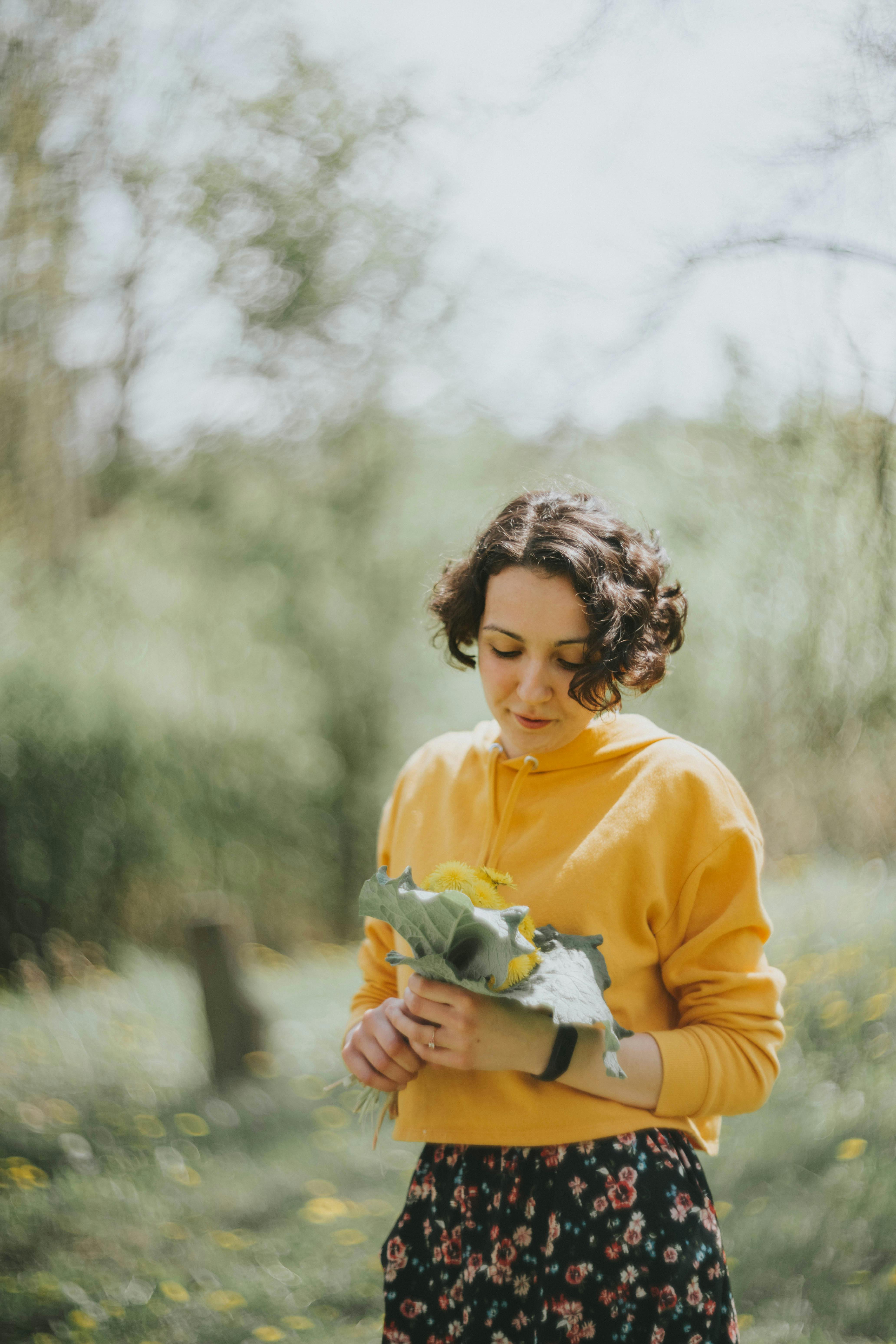 Young woman in yellow sweater holding flowers in a serene outdoor setting, reflecting tranquility and nature.