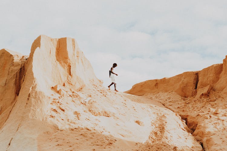 Person In White Tank Top Walking On Desert Hill