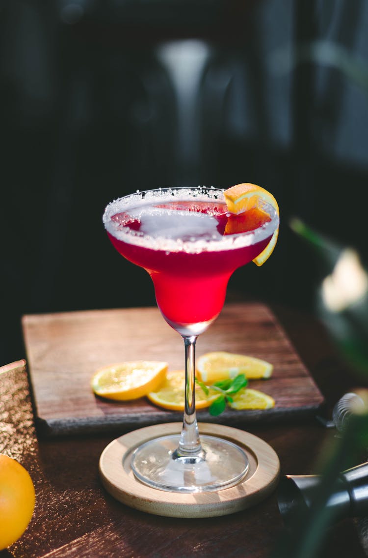 Shot Of A Pink Cocktail And Orange Slices On Bar Table