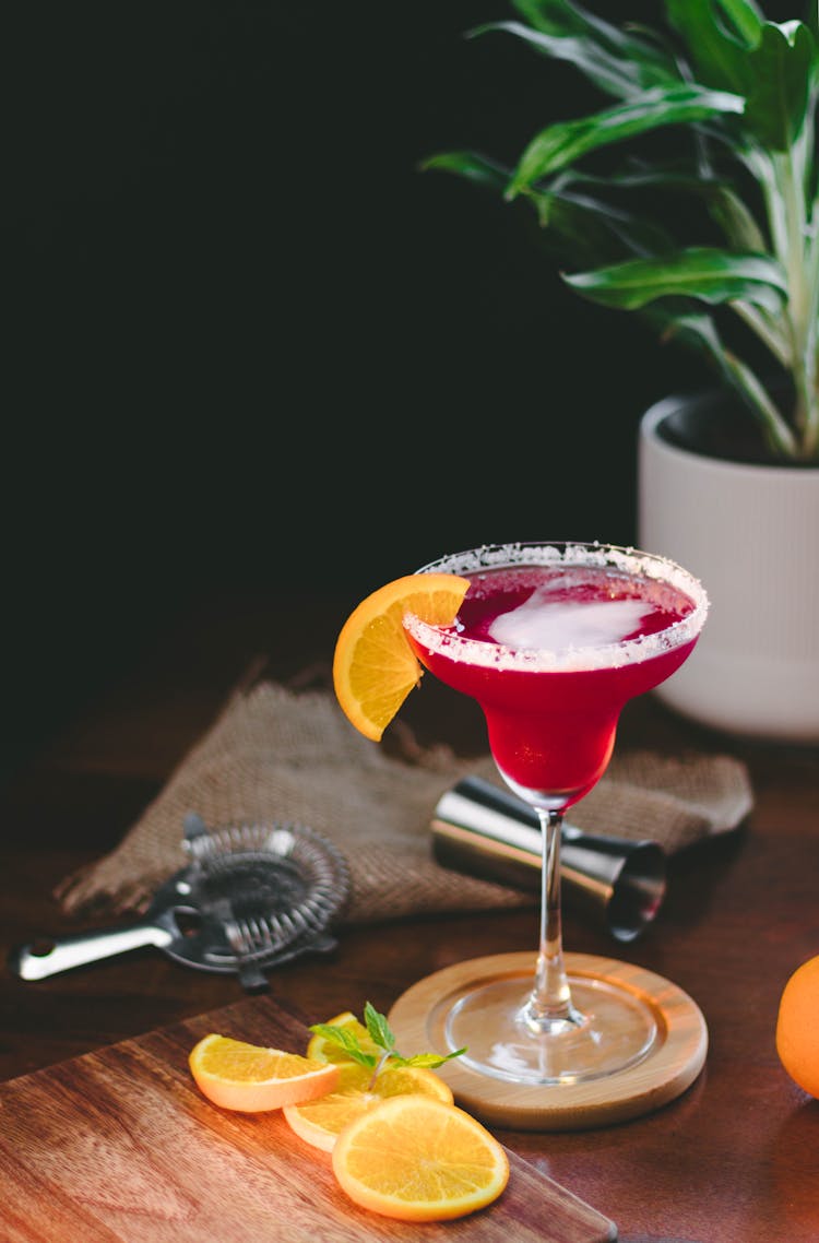 Shot Of A Pink Cocktail And Orange Slices On Bar Table