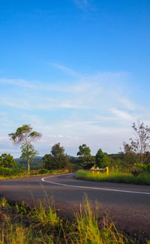 A peaceful winding road through the lush countryside under a clear blue sky in West Java, Indonesia.