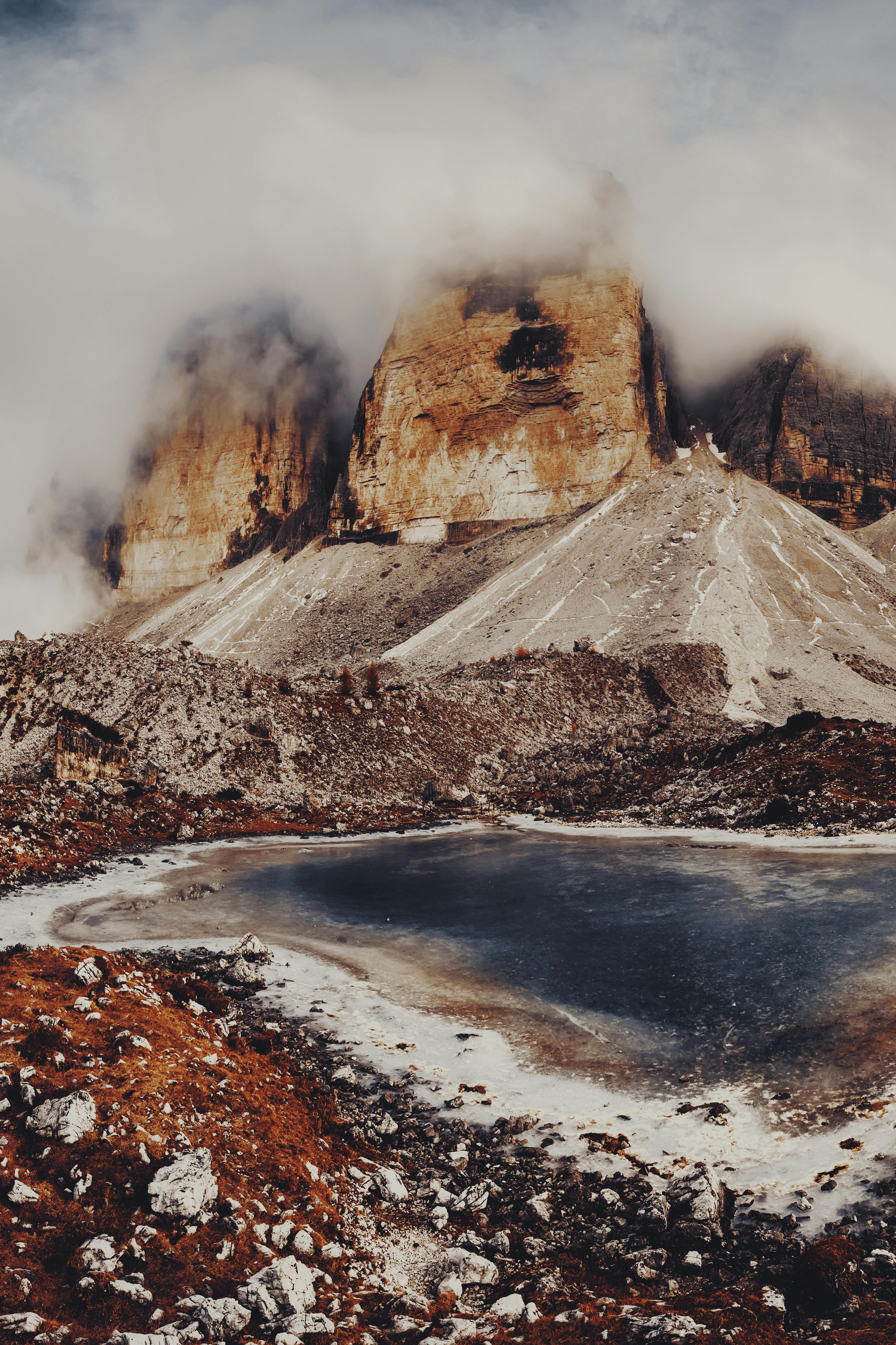 Stunning mountain landscape with misty cloud-covered peaks and a serene lake in winter.
