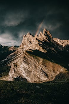 Majestic mountain range under stormy skies with a rainbow.