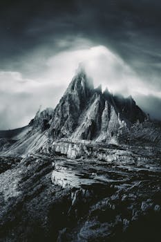 A striking monochrome photo of a rocky mountain peak under an overcast sky, exuding a sense of mystery.