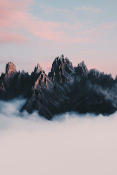 Stunning view of sharp Dolomite peaks piercing through clouds during a surreal sunset.