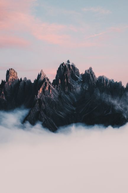 Stunning view of sharp Dolomite peaks piercing through clouds during a surreal sunset.