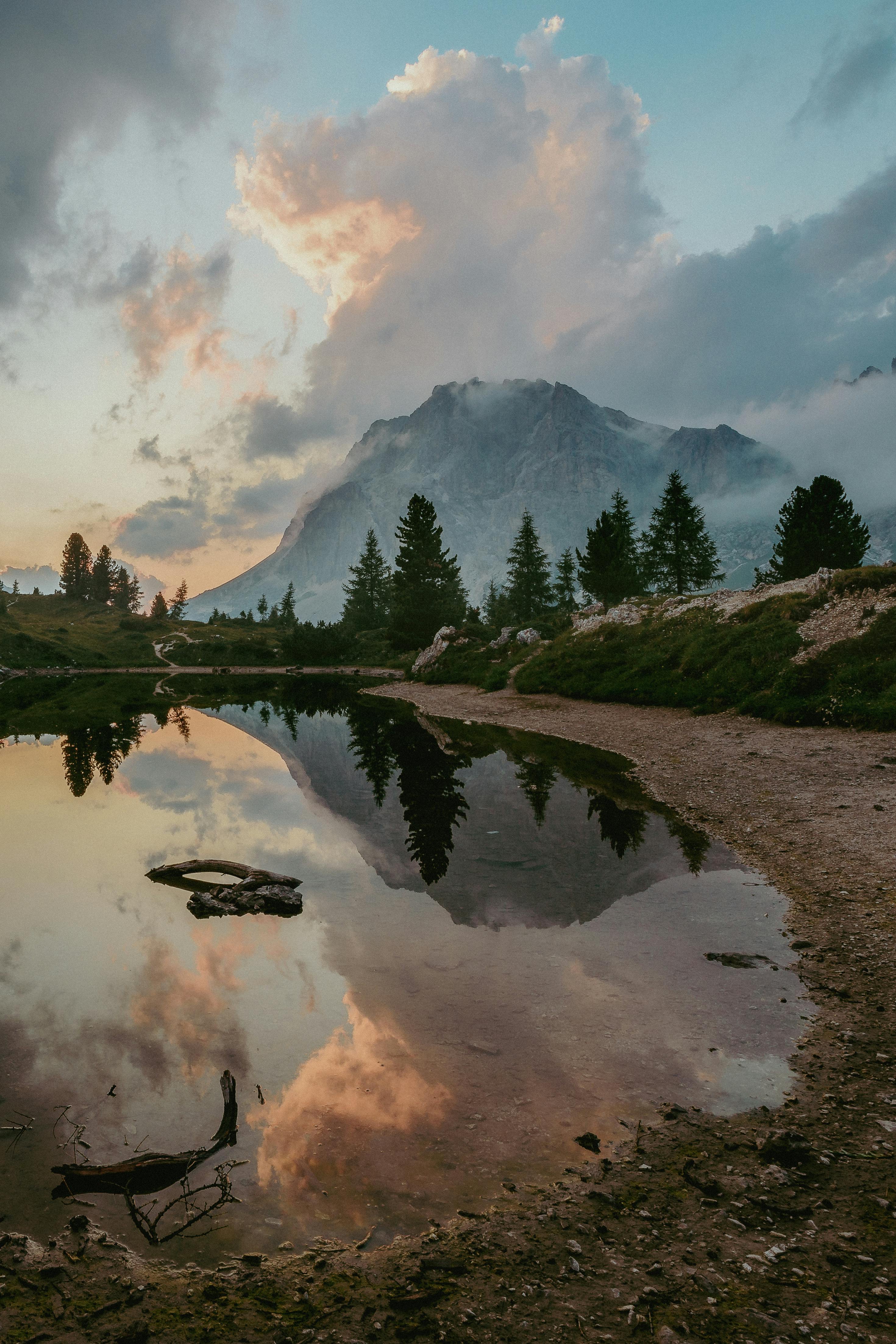 Stunning mountain landscape with lake reflection during sunrise, featuring trees and dramatic clouds.