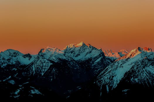 Stunning snow-covered mountains at sunset with an orange sky backdrop.