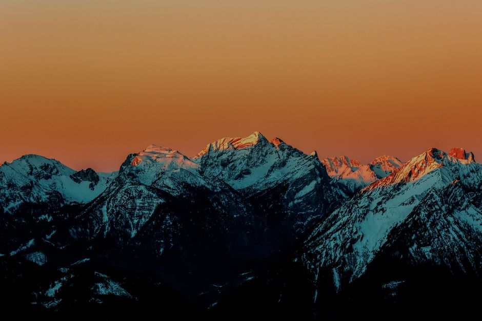 Stunning snow-covered mountains at sunset with an orange sky backdrop.