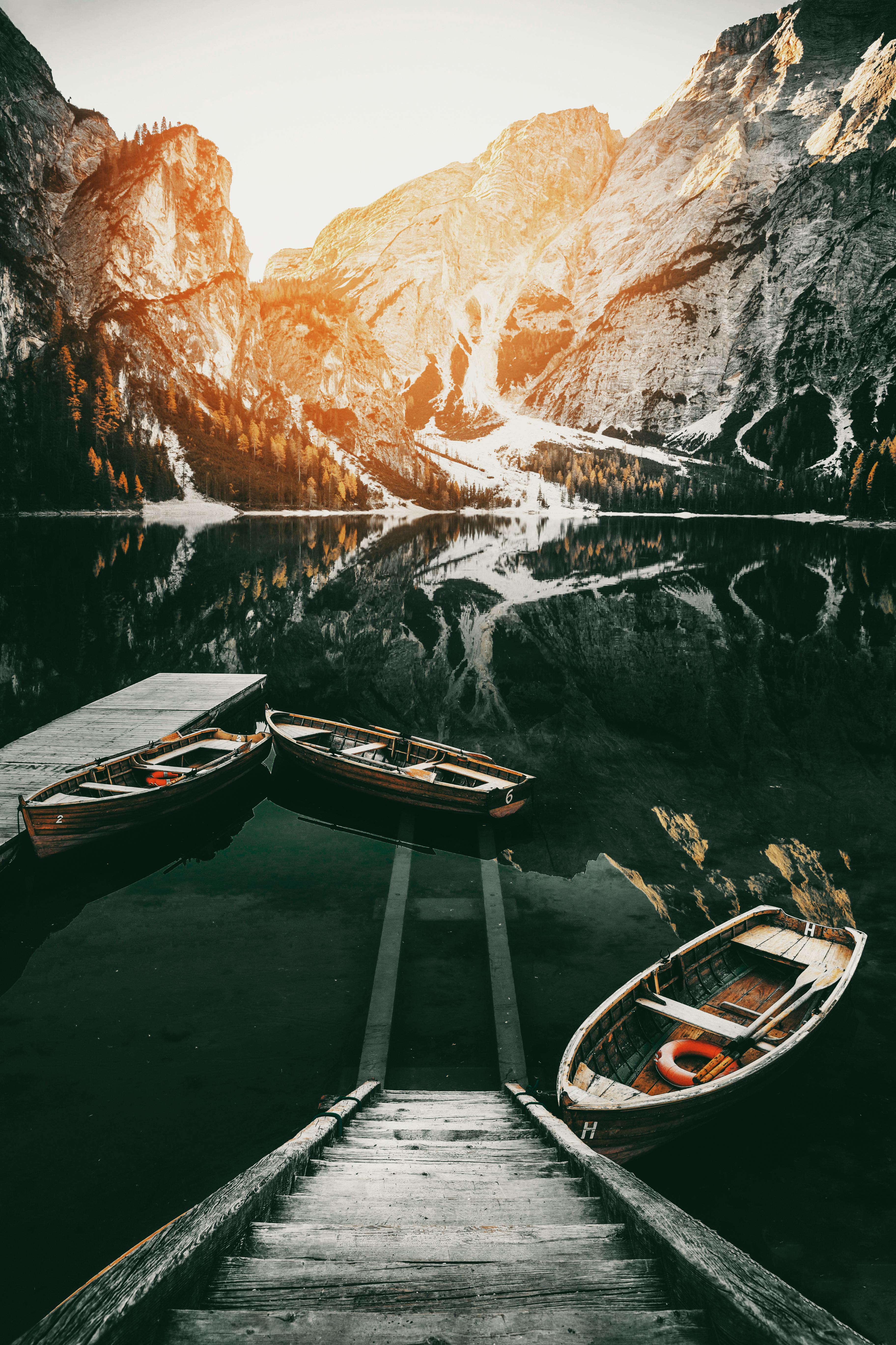 Tranquil mountain lake view with moored boats and snowcapped peaks at sunrise.