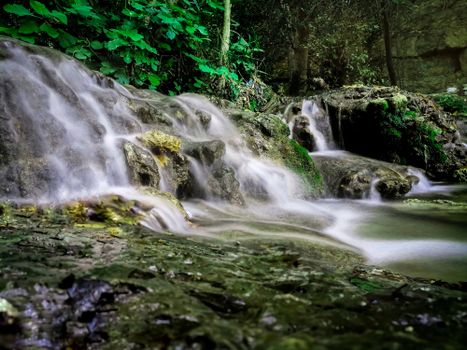 Tranquil waterfall cascading over rocks amidst lush green foliage in a peaceful forest setting.