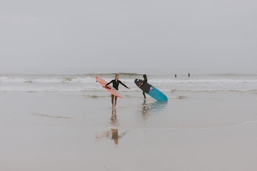 Fotografi Orang Di Seashore Holding Surboard