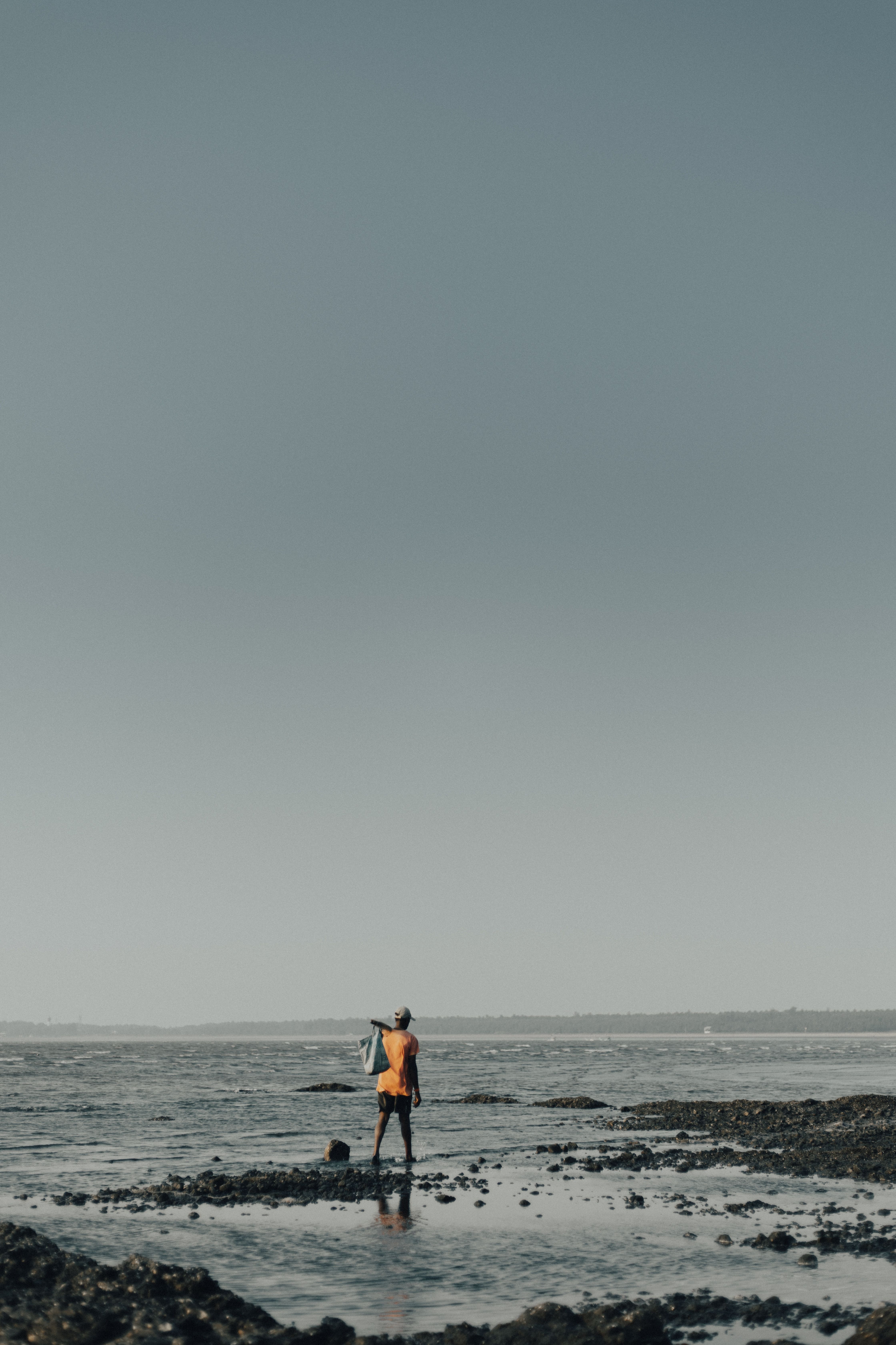 A solitary man in colorful attire walks along the rocky shore at Shirgaon Beach, India.